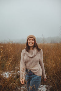 Portrait of smiling young woman standing on field against sky during winter