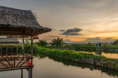 Gazebo by lake against sky during sunset