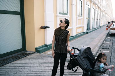 Woman standing with baby carriage in city