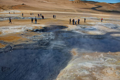 High angle view of people standing by hot spring on field during sunny day