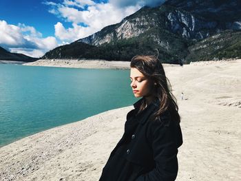 Beautiful young woman standing by lake and mountains