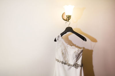 Wedding dress hanging on illuminated lamp by wall