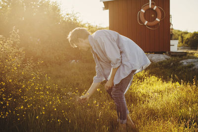 Side view of young man looking at flowers on sunny day