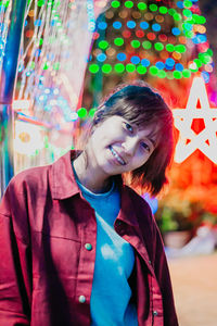 Portrait of smiling young woman against illuminated multi colored lighting equipment