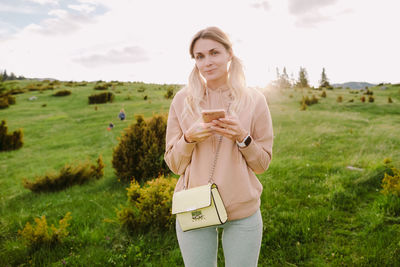 Young woman using phone while standing on field