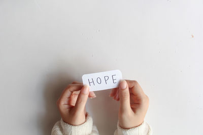 Cropped hand of person holding text against white wall