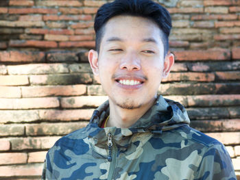 Portrait of smiling young man against brick wall