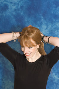 Young woman tying hair against blue wall