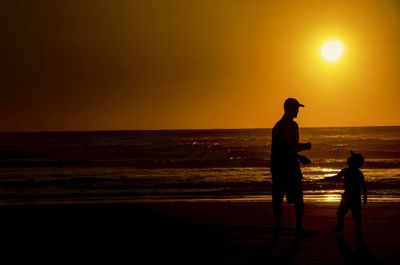 Silhouette people standing on beach against sky during sunset