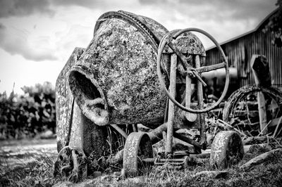Abandoned and rusty cement mixer on field against sky