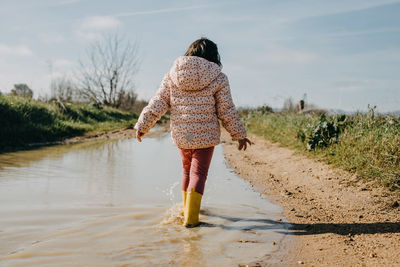 Rear view girl walking on a puddle with rubber boots