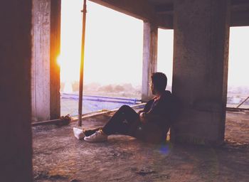 Side view of young man sitting on terrace against clear sky during sunset