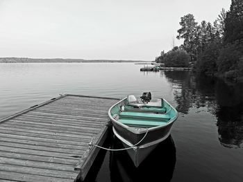 Boat moored on pier by lake against sky