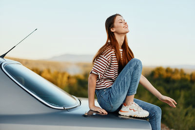 Portrait of young woman sitting on car