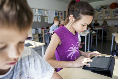 Girl sitting by boy while using digital tablet in classroom