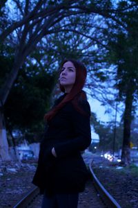 Young woman looking away while standing against trees