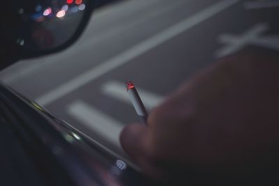 Cropped hand holding cigarette in car at night