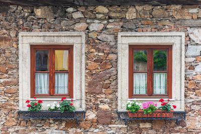 A wooden, brown windows and a fragment of a stone wall of the building. curtains hanging in window