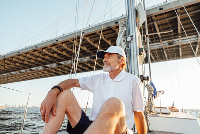 Senior man sitting on sailboat in sea against sky