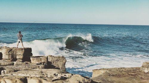 Man standing on rock by sea against clear sky