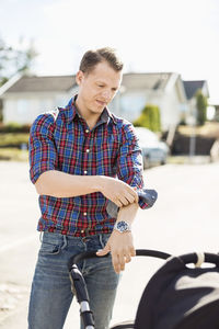 Man rolling up shirt sleeve while looking at baby carriage on street