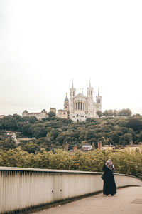 Rear view of person by cross against clear sky