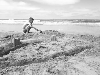 Boy playing with sand at beach against sky