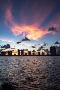 Sea by cityscape against sky during sunset