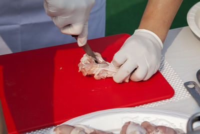 Midsection of chef cutting chicken meat on board