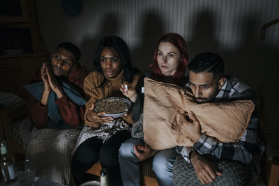 Multiracial male and female friends watching scary movie in cabin