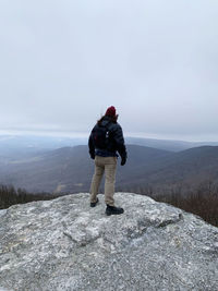 A young man looking over mountains from atop a rocky cliff