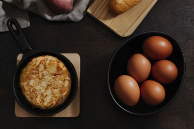 Spanish potato omelette with some fresh eggs shot from above over a wooden surface in a dark still life picture.