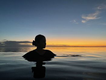 Rear view of woman standing in the sea against sky during sunset