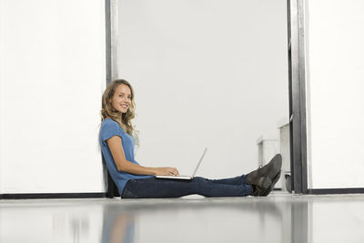 Casual businesswoman in office sitting on floor, using laptop