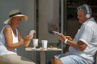 Couple using mobile phone and digital tablet while sitting at sidewalk cafe