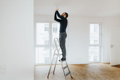 Home owner standing on ladder fixing light installation