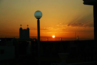 Silhouette street light by building against orange sky