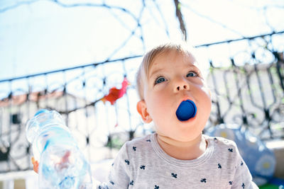 Low angle view of cute boy eating bottle cap outdoors