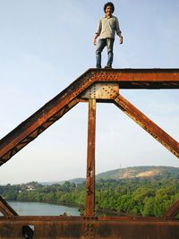 Low angle view of man standing on rusty metallic borim bridge against sky