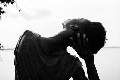 Rear view of young woman stretching neck against sky