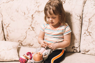 Child learns to tie shoelaces at home by playing with a doll. girl tying ties on doll clothes. 