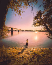 Rear view of man standing by river during sunset