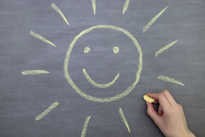 Cropped hand of woman drawing sun on blackboard