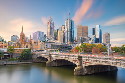 Bridge over river by buildings against sky in city