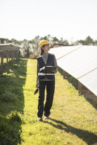 Female engineer looking away while walking amidst solar panels at power station