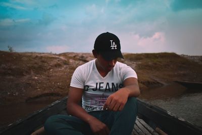 Young man sitting on shore against sky