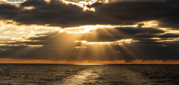 Sunlight streaming through clouds over sea at sunset