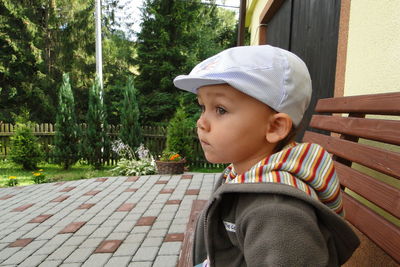 Side view of boy wearing flat cap while sitting on bench