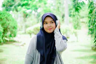 Beautiful young asian muslim woman listening to music with headphones in a park