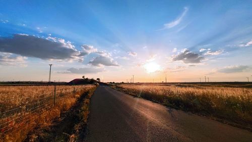 Road amidst field against sky during sunset